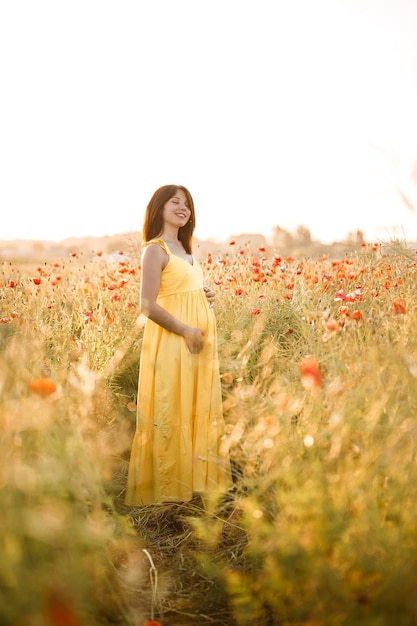 Mulher jovem e bonita em um vestido amarelo, andando em um campo de papoulas em um dia de verão. Menina apreciando flores na zona rural. Foco seletivo