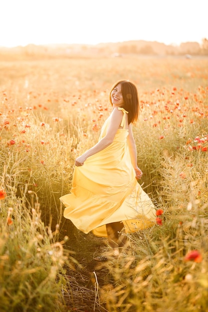 Mulher jovem e bonita em um vestido amarelo, andando em um campo de papoulas em um dia de verão. Menina apreciando flores na zona rural. Foco seletivo