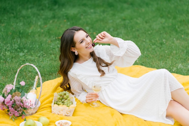Mulher jovem e bonita em um vestido branco bebendo vinho no jardim em um piquenique