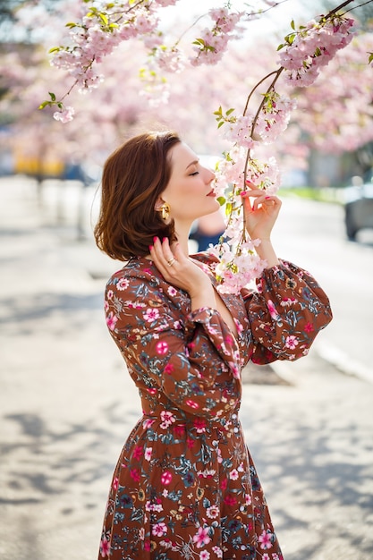 Mulher jovem e bonita em um vestido em árvores florescendo de sakura. É um dia quente e ensolarado de primavera lá fora