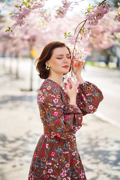 Mulher jovem e bonita em um vestido em árvores florescendo de sakura. É um dia quente e ensolarado de primavera lá fora