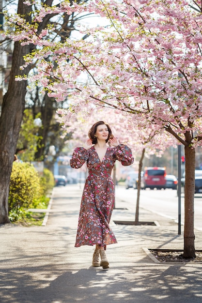 Mulher jovem e bonita em um vestido em árvores florescendo de sakura. É um dia quente e ensolarado de primavera lá fora