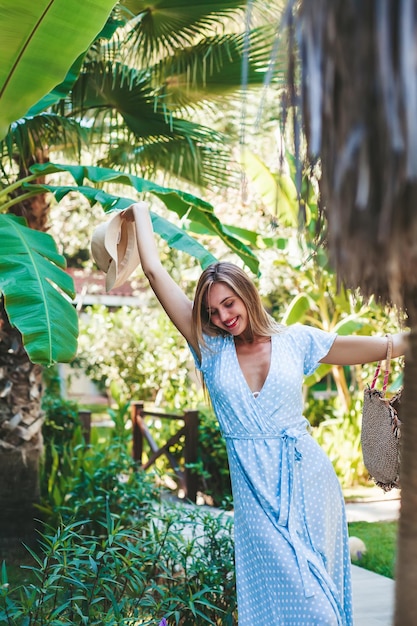 Mulher jovem e bonita em um vestido longo azul se sentindo feliz e livre em um jardim tropical verde