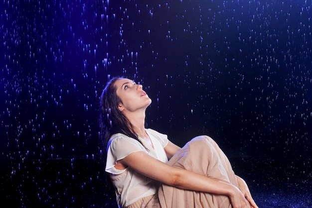 Mulher jovem e bonita em um vestido molhado na chuva atirando no estúdio em um fundo preto