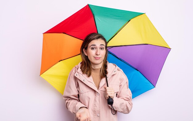 Mulher jovem e bonita encolhendo os ombros, sentindo-se confusa e incerta. conceito de guarda-chuva