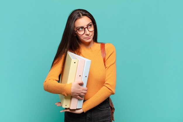 Mulher jovem e bonita encolhendo os ombros, sentindo-se confusa e incerta, duvidando com os braços cruzados e olhar perplexo. conceito de estudante