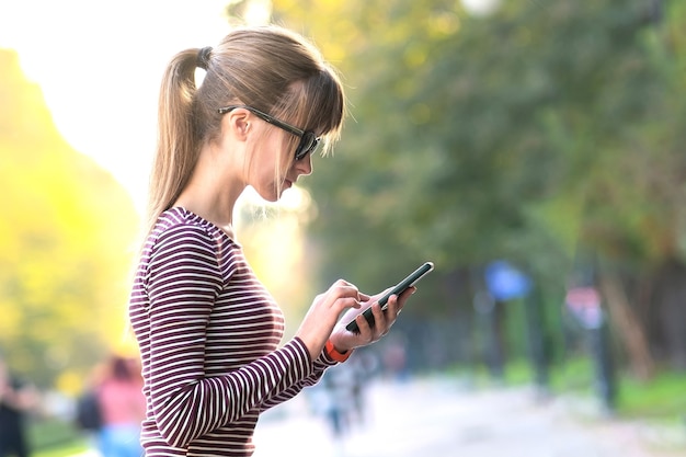 Mulher jovem e bonita enviando mensagens no celular em um dia quente de outono em uma rua ao ar livre da cidade.