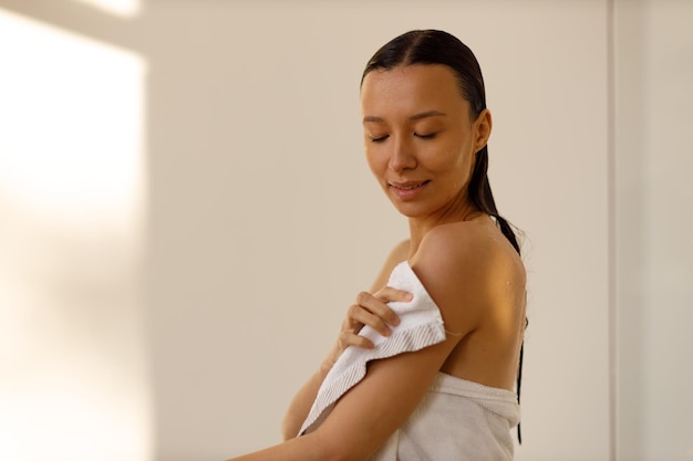 Foto mulher jovem e bonita envolvendo-se em toalha de banho branca no chuveiro higiene frescura e cuidados com o corpo cosméticos saudáveis
