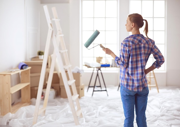 Mulher jovem e bonita fazendo pintura de parede em pé perto da escada