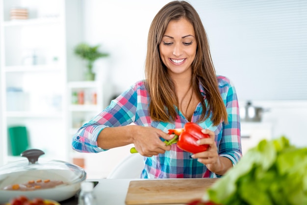 Mulher jovem e bonita fazendo refeição saudável na cozinha doméstica. Ela prepara pimenta para recheio.