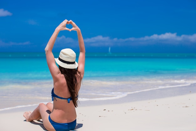 Mulher jovem e bonita fazendo um coração com as mãos na praia