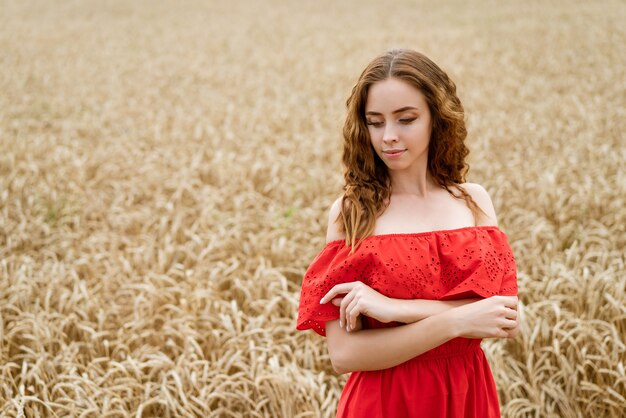 Mulher jovem e bonita feliz com cabelo encaracolado em um vestido vermelho, posando em um campo de trigo.