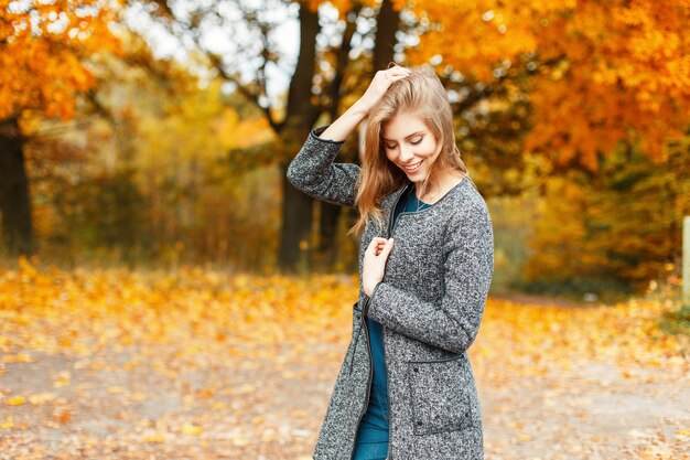 Mulher jovem e bonita feliz com um casaco elegante no parque outono amarelo