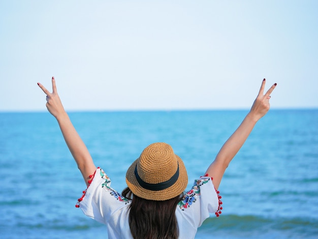 Foto mulher jovem e bonita feliz com um chapéu, desfrutando de liberdade, relaxe e feliz na praia. conceito de viagens de verão.