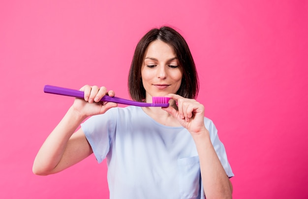 Mulher jovem e bonita feliz com uma escova de dentes grande em um fundo rosa em branco