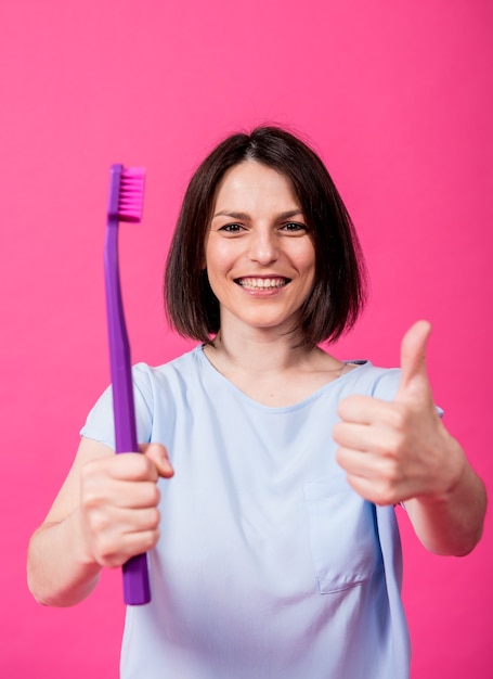 Mulher jovem e bonita feliz com uma escova de dentes grande em um fundo rosa em branco