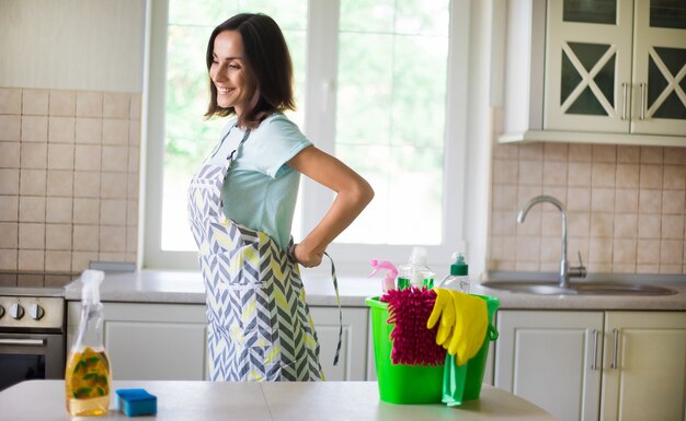 Mulher jovem e bonita feliz em luvas amarelas está limpando a cozinha com equipamento especial e spray