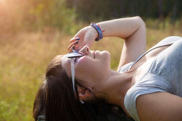 Mulher jovem e bonita feliz em óculos de sol sorri e deita-se em um prado na grama ao sol