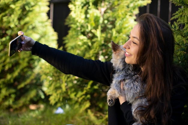 Mulher jovem e bonita feliz se divertindo ao ar livre, fazendo selfie no celular com o cachorrinho de estimação