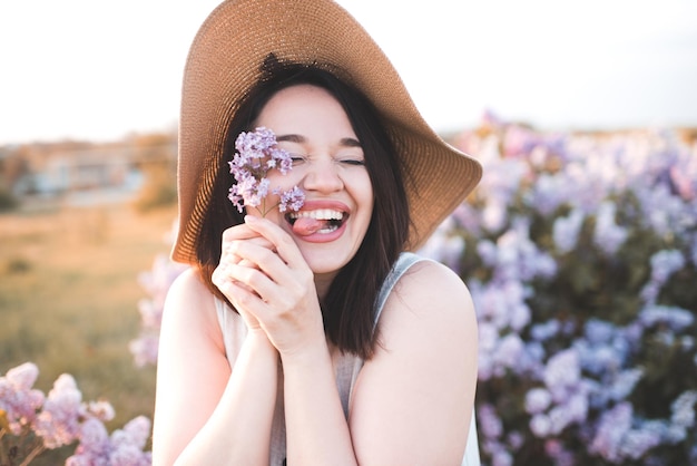 Mulher jovem e bonita feliz se divertindo segurando uma flor lilás com chapéu de palha