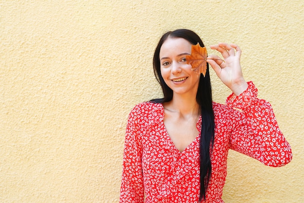 Mulher jovem e bonita feliz segurando folhas de outono. garota ao ar livre com vestido vermelho