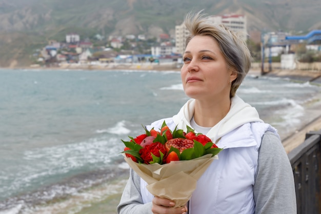 Mulher jovem e bonita fica à beira-mar com um buquê nas mãos