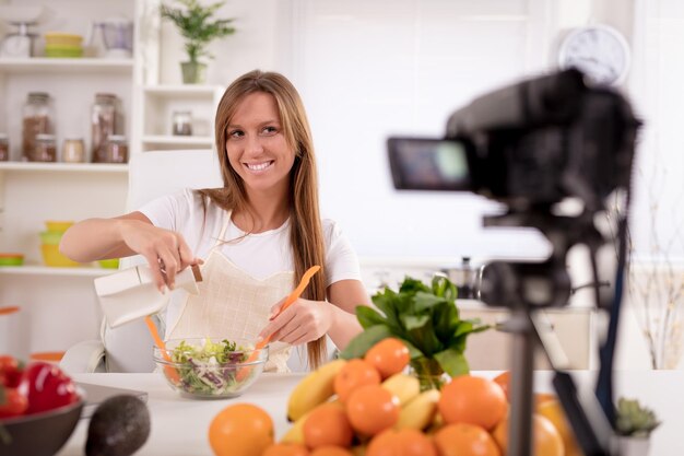 Mulher jovem e bonita filmando sua transmissão de blog sobre comida saudável em casa.