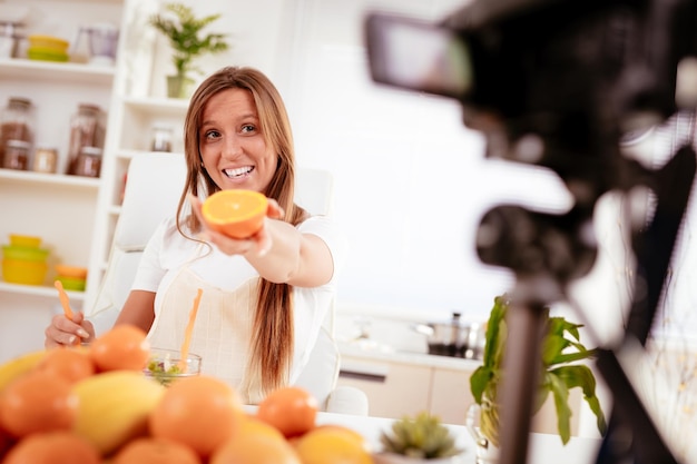 Mulher jovem e bonita filmando sua transmissão de blog sobre comida saudável em casa.