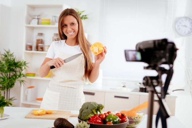 Mulher jovem e bonita filmando sua transmissão de blog sobre comida saudável em casa.