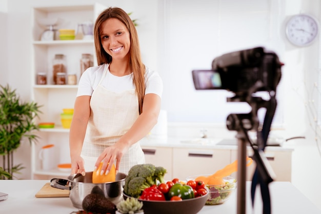 Mulher jovem e bonita filmando sua transmissão de blog sobre comida saudável em casa.