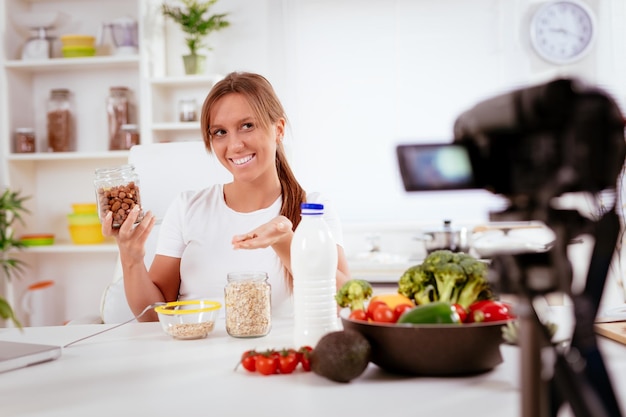 Mulher jovem e bonita filmando sua transmissão de blog sobre comida saudável em casa.