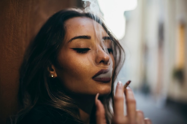 Mulher jovem e bonita fuma cigarro fora da cidade.