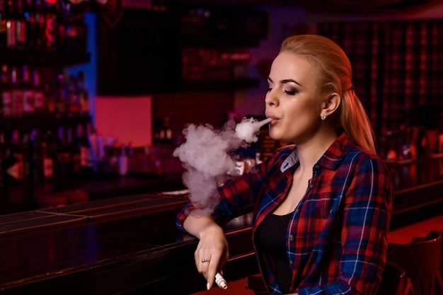 Mulher jovem e bonita fumando um cigarro eletrônico no bar vape