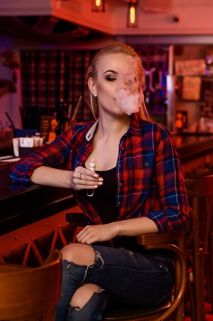 Mulher jovem e bonita fumando um cigarro eletrônico no bar vape