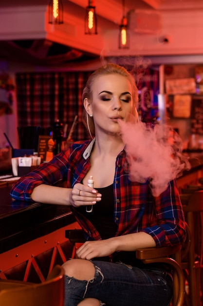 Mulher jovem e bonita fumando um cigarro eletrônico no bar vape