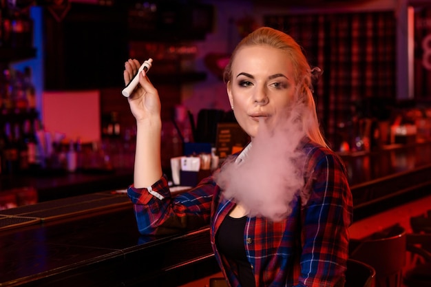 Mulher jovem e bonita fumando um cigarro eletrônico no bar vape