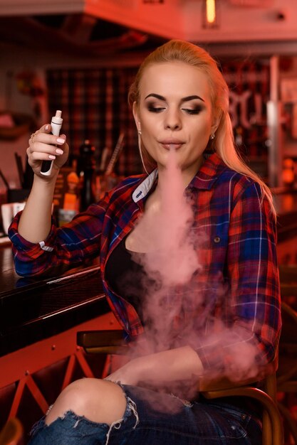 Mulher jovem e bonita fumando um cigarro eletrônico no bar vape