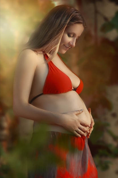 Mulher jovem e bonita grávida com a barriga nua caminhando na natureza perto da floresta e do lago