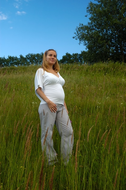 Mulher jovem e bonita grávida com uma barriga nua em pé no Prado. Gravidez na natureza colorida, ela gosta da natureza quente do verão