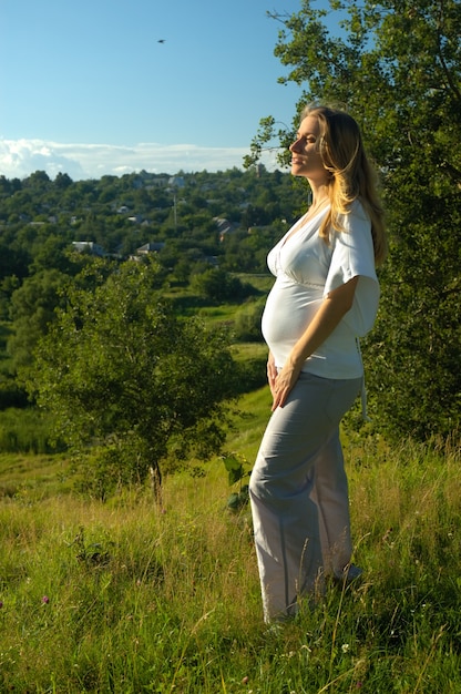 Mulher jovem e bonita grávida com uma barriga nua em pé no prado. gravidez na natureza colorida, ela gosta da natureza quente do verão