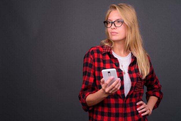 Mulher jovem e bonita hippie com cabelo loiro e óculos contra uma parede cinza