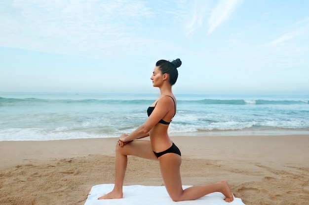 Mulher jovem e bonita incrível bonita fitness ao ar livre na praia fazer exercícios de esporte de ioga. Estilo de vida ativo. Conceito de saudável e ioga.