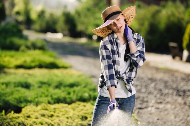 Mulher jovem e bonita jardineiro regando o jardim num dia quente de verão.