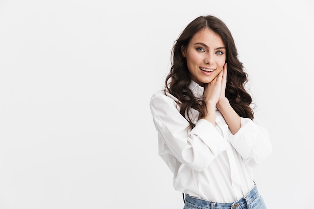 Mulher jovem e bonita linda com cabelo longo encaracolado morena, vestindo camisa branca em pé, isolado sobre uma parede branca