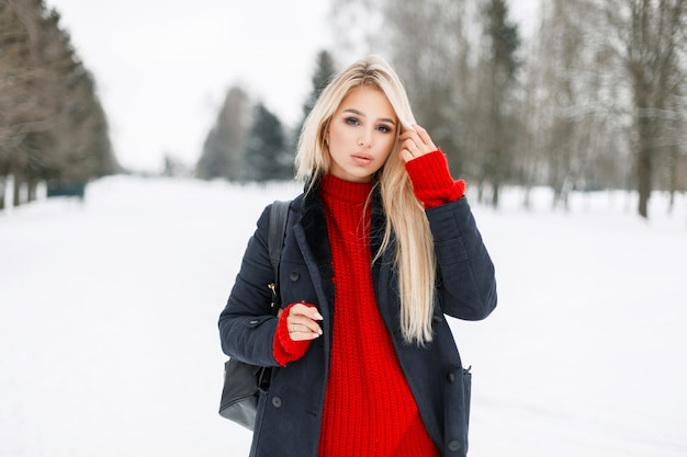 Mulher jovem e bonita loira com um elegante casaco de inverno caminhando ao ar livre em um dia de inverno