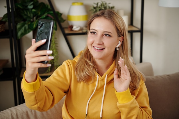 Mulher jovem e bonita loira usando fones de ouvido sem fio e um amigo de videochamada via smartphone