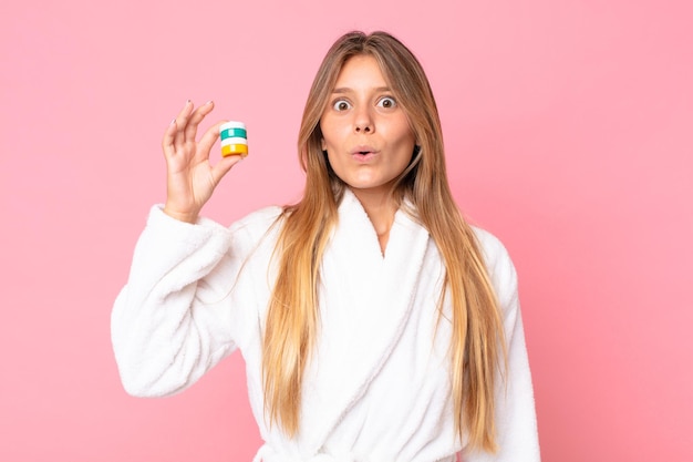 Mulher jovem e bonita loira vestindo roupão de banho e segurando um produto cosmético