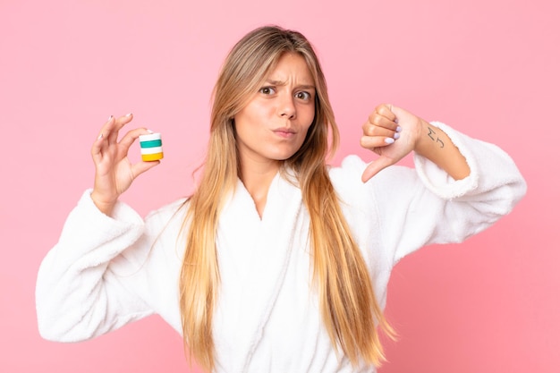 Mulher jovem e bonita loira vestindo roupão de banho e segurando um produto cosmético