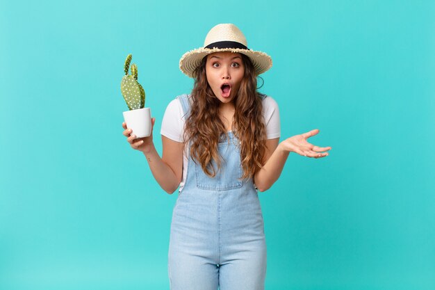 Mulher jovem e bonita maravilhada, chocada e atônita com uma surpresa inacreditável e segurando um cacto