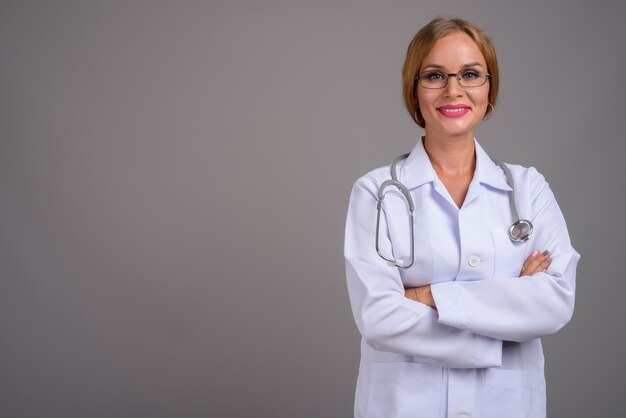 Mulher jovem e bonita médica com cabelo loiro contra fundo cinza